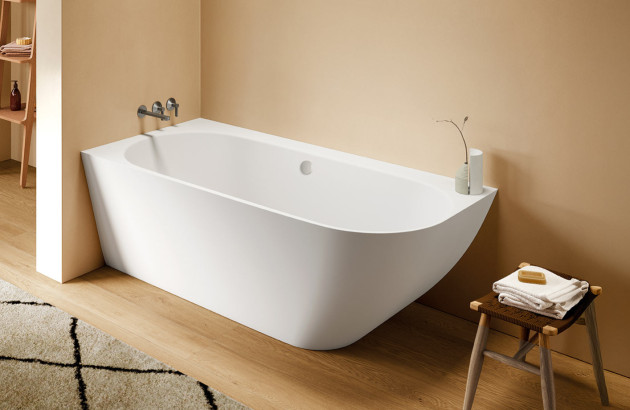 Baignoire blanche adossée au mur avec angle arrondi dans une salle de bains chaleureuse aux tons beige.