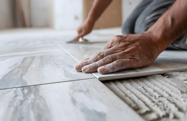Pose de carrelage de sol grand format par un artisan lors d’un chantier de rénovation.