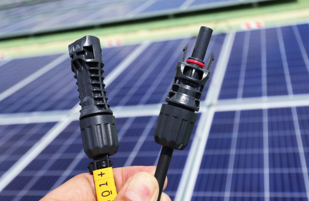 Personne qui tient 2 cables avec des panneaux solaires à l'arrière plan