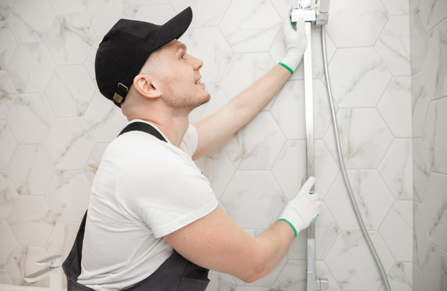 un professionnel installant une douche dans une salle de bains carrelée marbre blanc