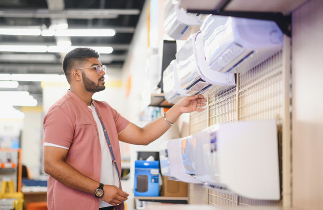 homme qui regarde et touche un climatiseur mural blanc exposé dans un magasin d'électroménager