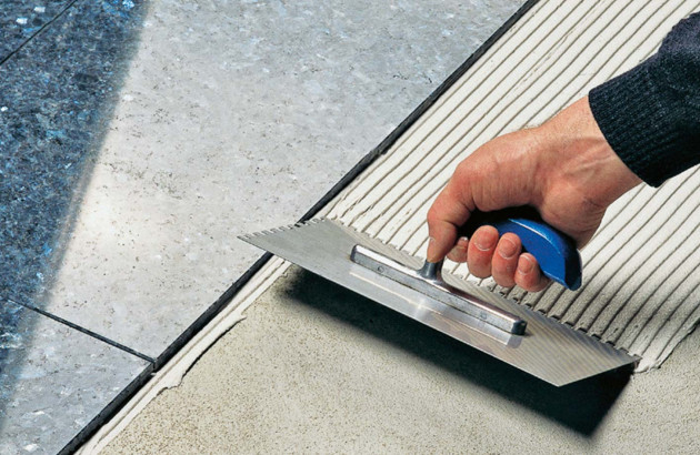 Homme qui utilise une taloche pour strier la colle de carrelage