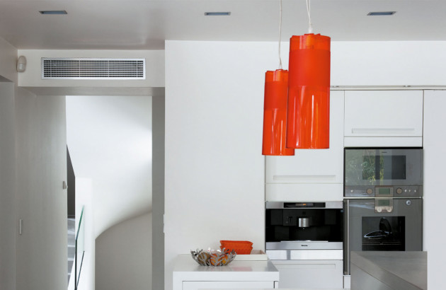 grille de climatisation placé au dessus de l'encadrement de porte, dans une cuisine blanche avec des luminaires gris.