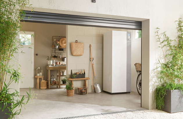Module intérieur de pompe à chaleur Atlantic installé dans un garage lumineux avec rangements et outils de jardinage.