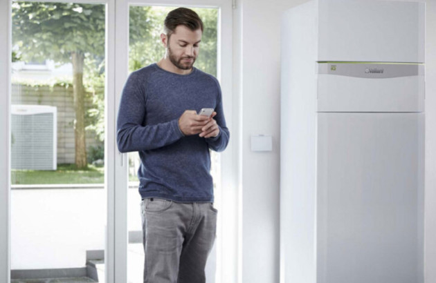 Homme qui regarde son téléphone à côté de l'unité intérieure de sa pompe à chaleur