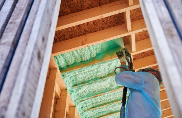  ouvrier en équipement de protection applique de l'isolant en mousse pulvérisée verte sur la structure en bois d'un bâtiment