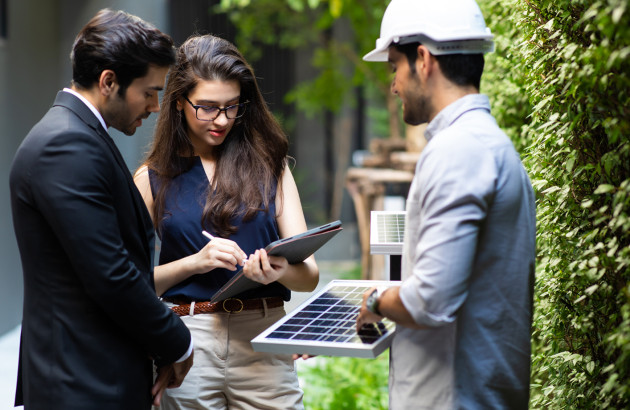Conseiller expliquant un projet d’installation de panneaux solaires à des particuliers en extérieur.