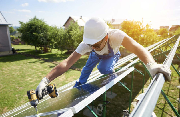 Installateur de panneaux solaires qui visse une vis sur d'un panneau sur son support, à l'aide d'une visseuse
