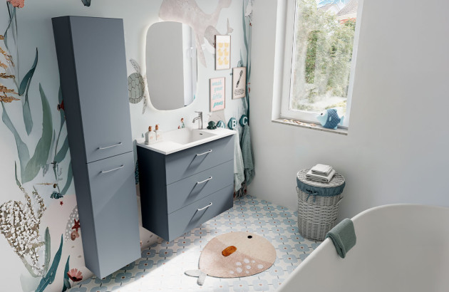 Salle de bains enfant avec meuble sous vasque bleu, papier peint marin et nombreux rangements adaptés à la famille.