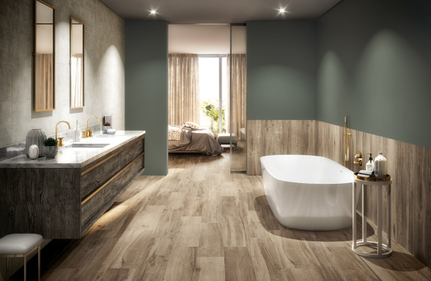 Salle de bains contemporaine avec carrelage de sol imitation bois, baignoire îlot blanche et meuble double vasque aux finitions dorées.