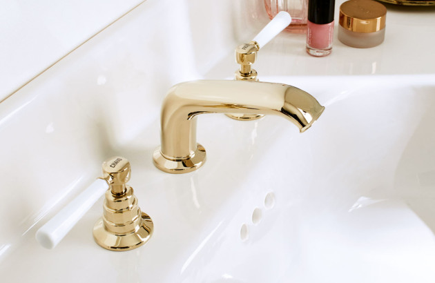 Robinetterie de lavabo vintage en finition dorée brillante avec poignées blanches inspirées des salles de bains traditionnelles.