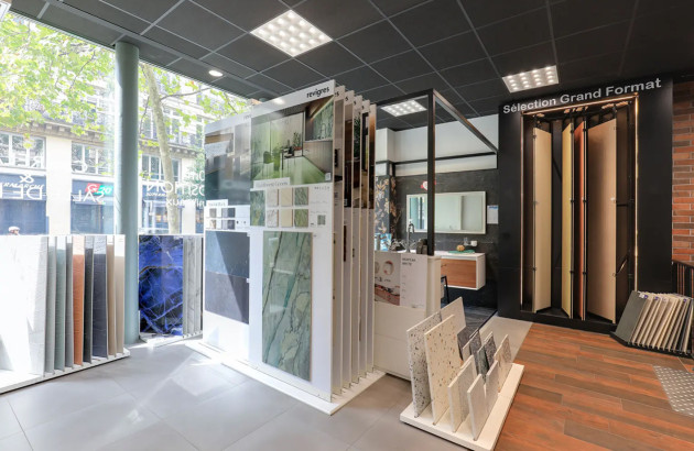Showroom carrelage avec grands panneaux et échantillons de grès cérame gris, espace d’inspiration pour vos projets.