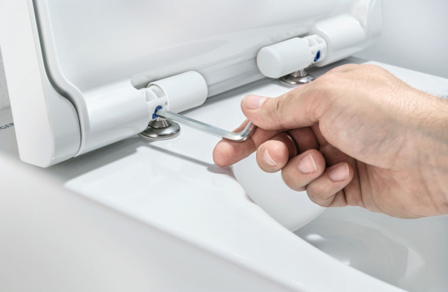 Réglage de la fixation d’un abattant sur WC suspendu sans bride à l’aide d’une clé Allen, détail des charnières et système de fixation pour une installation précise et stable.