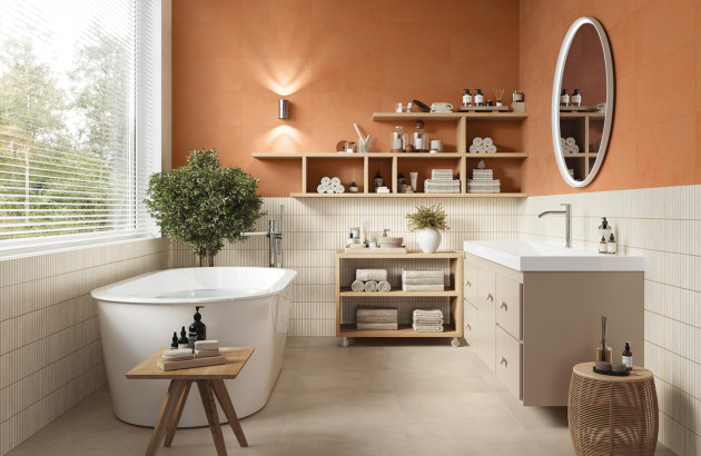 Salle de bains chaleureuse avec carrelage mural terracotta, faïence blanche striée, baignoire îlot et mobilier en bois clair.