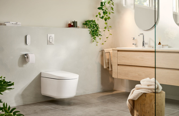 Salle de bains naturelle avec WC suspendu blanc, meuble vasque en bois clair et plantes vertes.