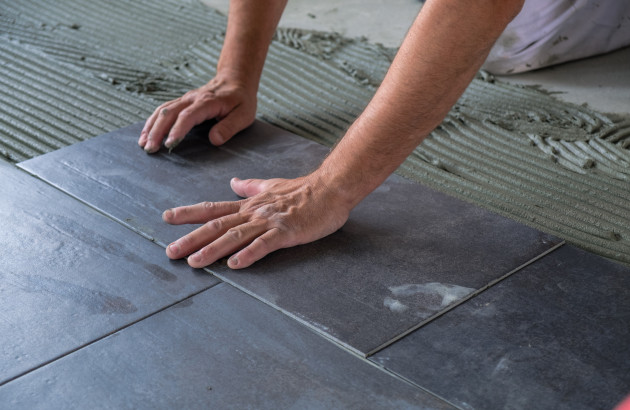 Homme qui pose des grands carreaux de carrelage avec du mortier colle
