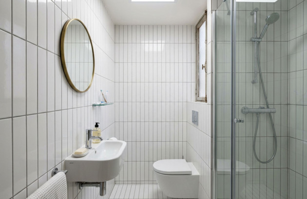 Petite salle de bains entièrement habillée de carrelage mural blanc vertical avec douche vitrée.