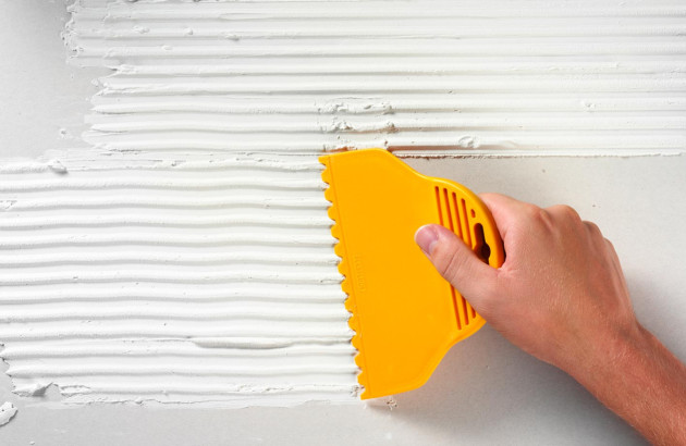 Homme qui utilise une taloche jaune pour étaler de la colle de carrelage sur un support