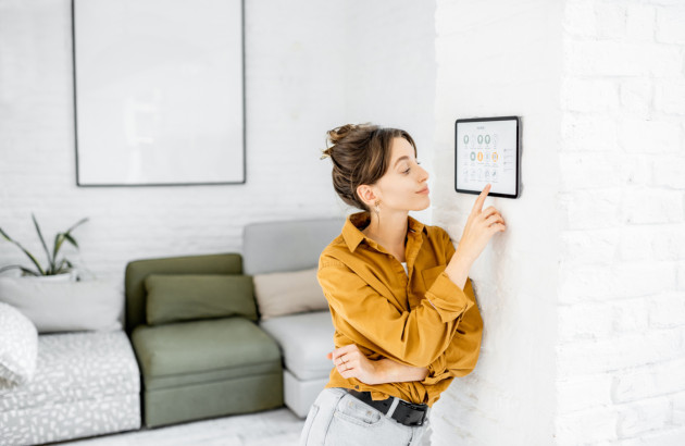 Femme utilisant un écran tactile mural pour contrôler les équipements et la consommation énergétique de sa maison connectée.