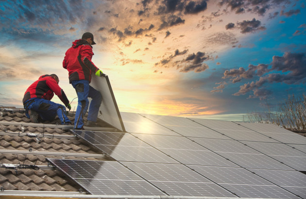 Deux installateurs fixant des panneaux solaires photovoltaïques sur la toiture d'une maison au coucher du soleil.