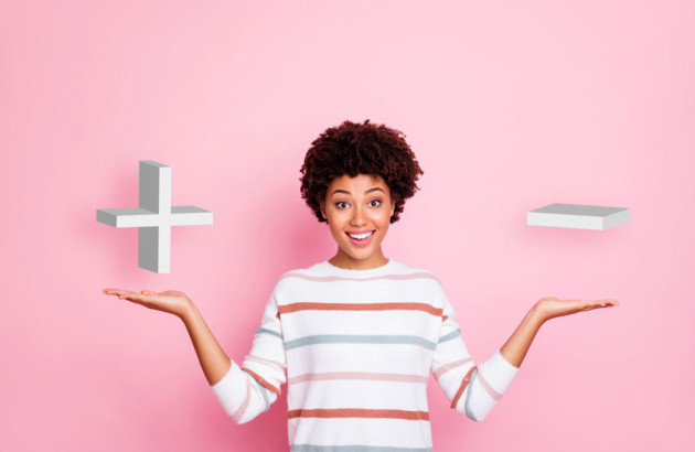Femme surélevant les signes + et -, le tout sur fond rose