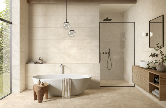 Grande salle de bains lumineuse avec baignoire îlot, douche à l’italienne et carrelage effet pierre dans des tons sable.