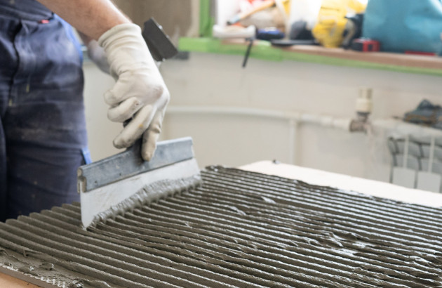 Homme qui applique du mortier colle sur un carreau de carrelage à l'aide d'un peigne