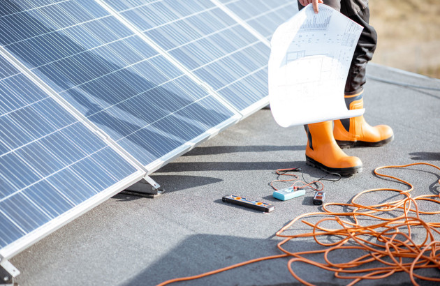 Artisan installateur de panneaux solaires sur un toit de maison avec un epi, devant une installation de panneaux