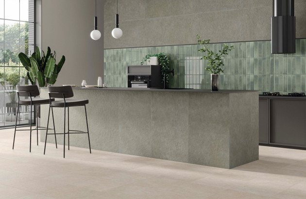 Cuisine contemporaine avec îlot central gris, crédence en carrelage vert sauge et sol carrelé beige clair.