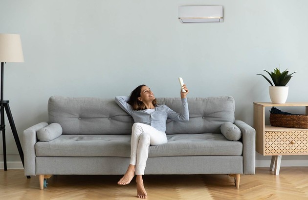 femme sur un canapé utilisant sa télécommande pour régler la climatisation