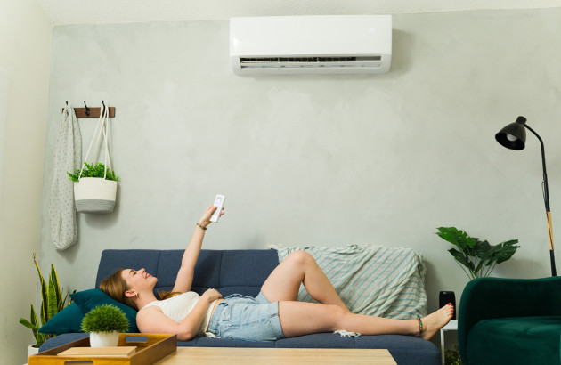 Femme utilisant une télécommande pour régler une climatisation murale dans un séjour confortable.