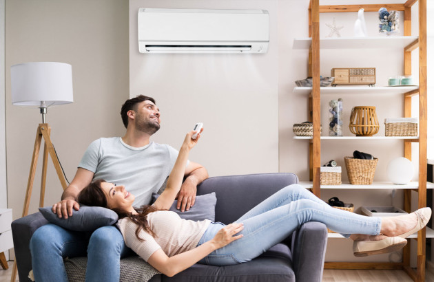 couple souriant se détend sur un canapé la femme utilisant une télécommande pour régler le climatiseur mural