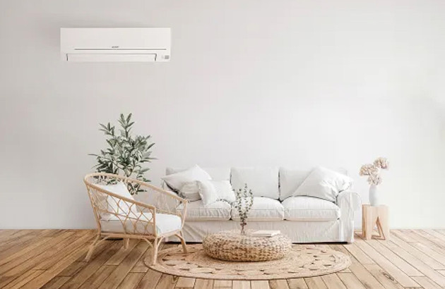 Climatiseur mural discret installé au-dessus d’un canapé dans un salon minimaliste aux tons clairs et naturels