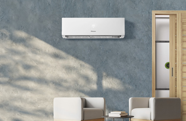 climatiseur mural blanc de marque Hisense installé sur un mur texturé gris près de deux fauteuils modernes beiges clairs