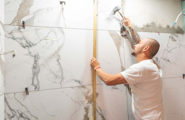 Homme qui colle des carreaux de carrelage XXL imitation marbre sur le mur