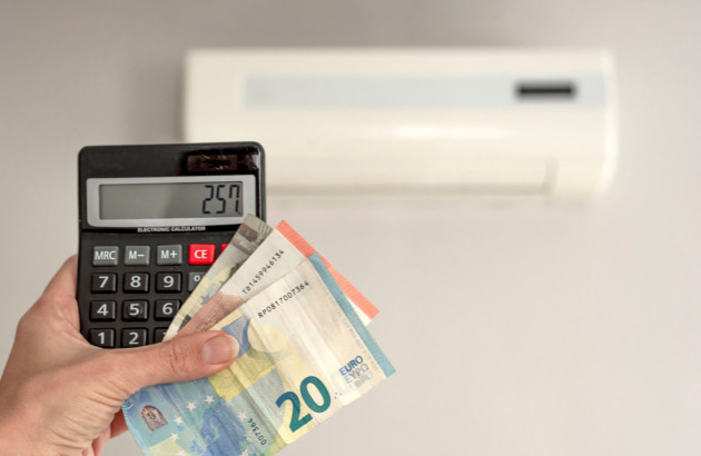 Calculatrice et billets devant une climatisation murale illustrant le coût de l’entretien ou de la maintenance d’une climatisation.