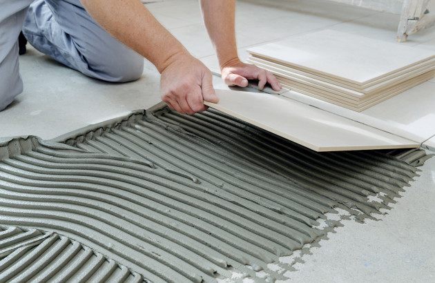 Homme qui pose un carreau de carrelage sur le sol avec du mortier colle