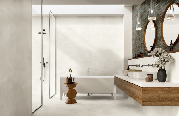 Salle de bains zen habillée de carrelage beige effet pierre, avec baignoire îlot blanche, douche à l’italienne et meuble vasque suspendu en bois.