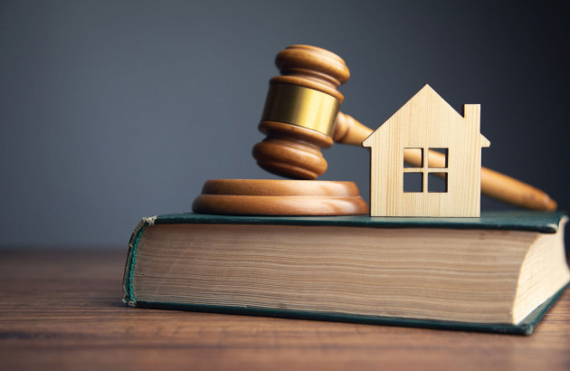 Marteau de juge en bois avec une maison en bois posés sur un livre