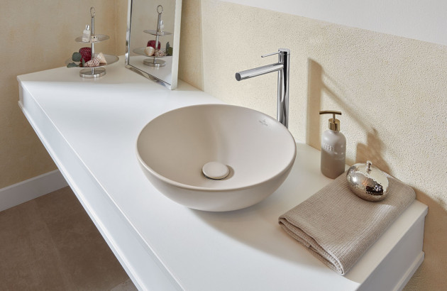 Vasque ronde beige à poser avec robinet haut chromé sur plan de toilette blanc.
