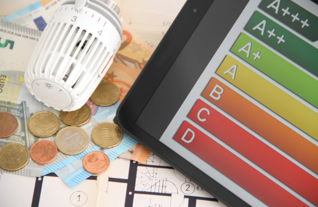 Thermostat de radiateur posé sur des billets et une tablette affichant une étiquette de performance énergétique.