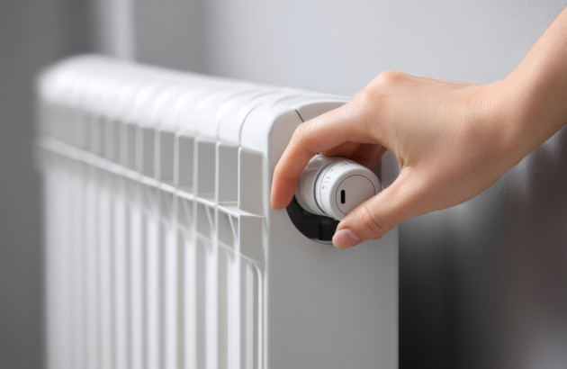 Main réglant le thermostat d’un radiateur blanc pour ajuster la température de chauffage.