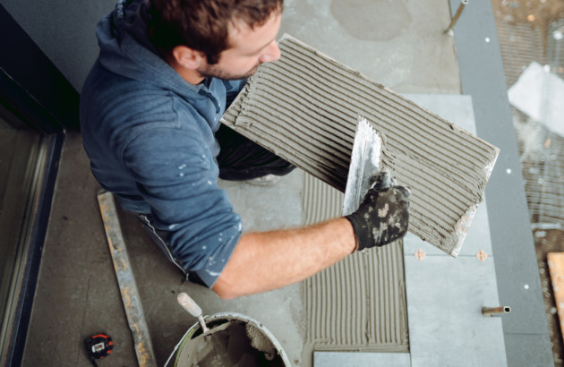 Homme artisan qui utilise un peigne à colle de carrelage pour appliquer du mortier sur un carreau