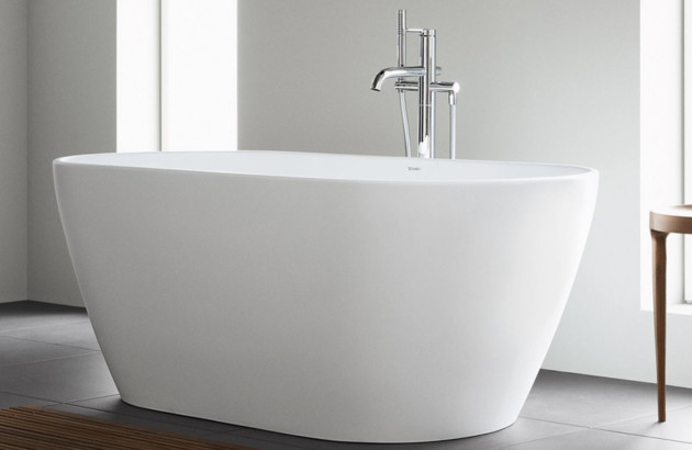 Baignoire îlot design en résine blanche avec robinetterie sur pied chromée.