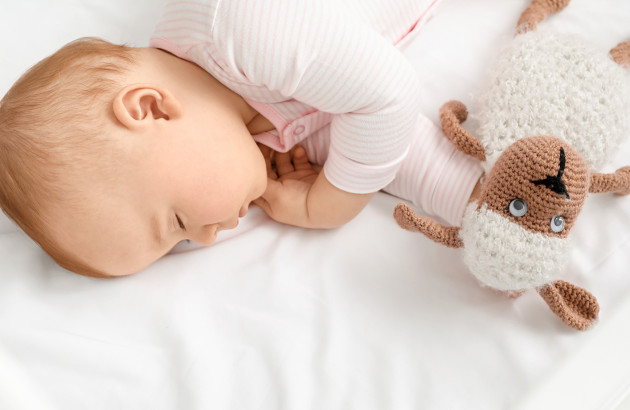 Bébé qui dort sur le côté dans un lit avec une peluche de vache