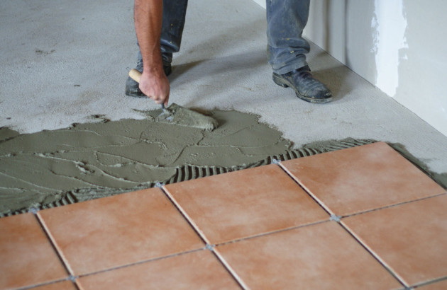 Homme qui tartine du mortier pour coller des carreaux de carrelage ocre