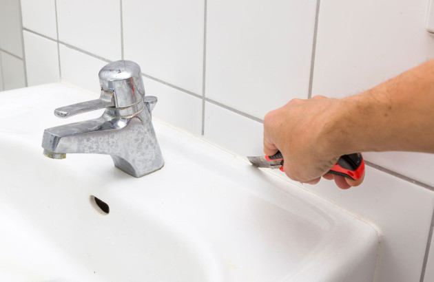 Homme qui utilise un cutter pour enlever le joint de son lavabo et carrelage