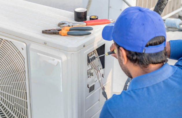 technicien qui utilise un tournevis pour travailler sur le panneau électrique ouvert d'une unité extérieure de climatisation avec des outils