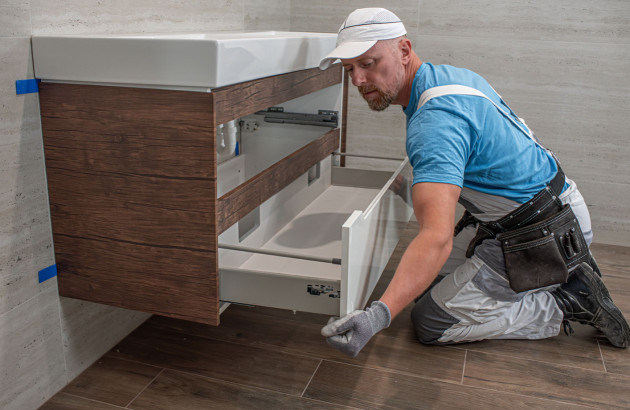 Professionnel installant un meuble sous vasque suspendu lors d’un chantier de rénovation de salle de bains.