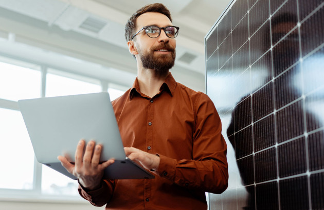 Homme qui tient un ordinateur devant un panneau solaire